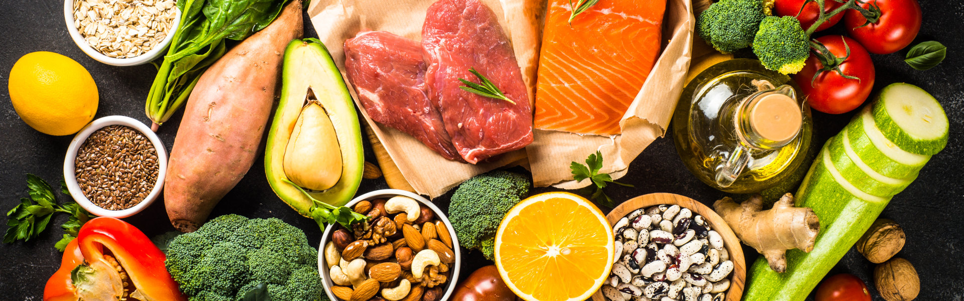 Gesunde Lebensmittel wie Gemüse, Obst, Nüsse, Fisch und Fleisch auf dunklem Untergrund